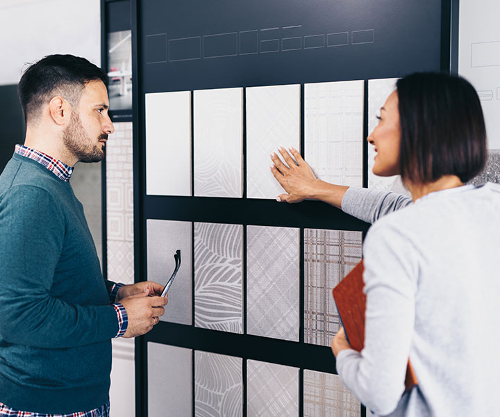 Beratungsgespräch vor einer Wand mit Fliesenmustern in verschiedenen Formaten